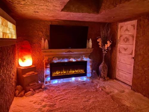 Cozy room with a faux fireplace, TV, salt lamps, and decorative elements, all set in a sandy, earthy environment.
