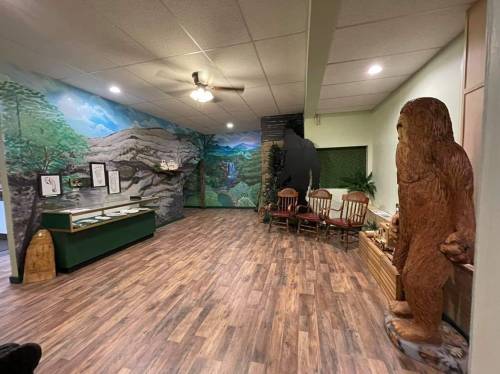 Interior of a room featuring a mural of mountains, wooden chairs, and a large Sasquatch statue.