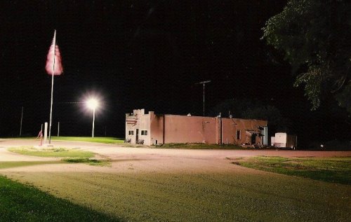 A dimly lit building at night with an American flag and a streetlight in a rural setting.