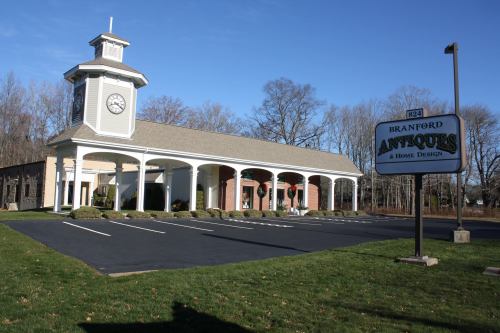 A building with a clock tower and a sign for Branford Antiques & Home Design, surrounded by a grassy area and trees.