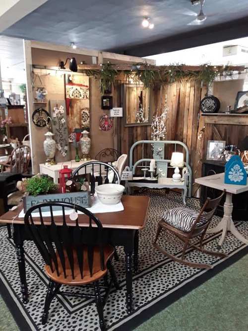 A cozy vintage-inspired room display featuring a wooden table, chairs, and decorative items on rustic walls.