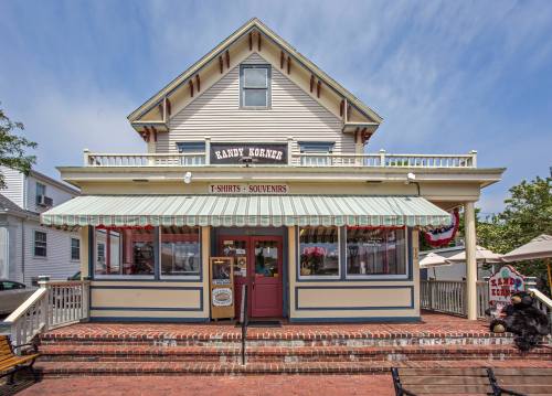 A charming storefront with a striped awning, featuring signs for t-shirts and souvenirs, surrounded by outdoor seating.