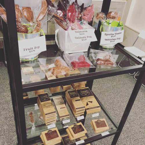 Display of colorful candy pops and chocolate treats in a glass case, labeled with prices and themes.