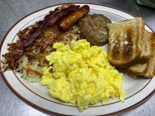 A plate of breakfast featuring scrambled eggs, hash browns, bacon, sausage, a sausage patty, and toast.