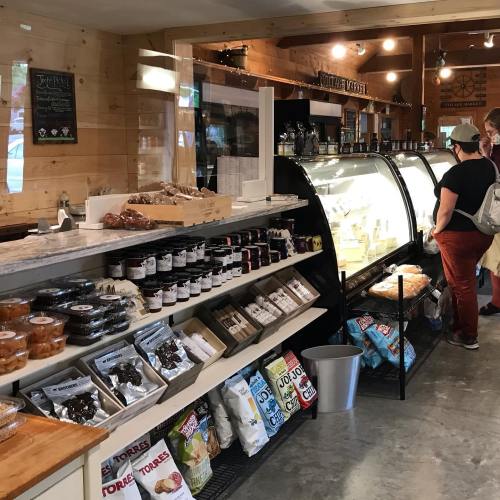 A cozy shop interior with wooden decor, showcasing a variety of jars, snacks, and a glass display case.