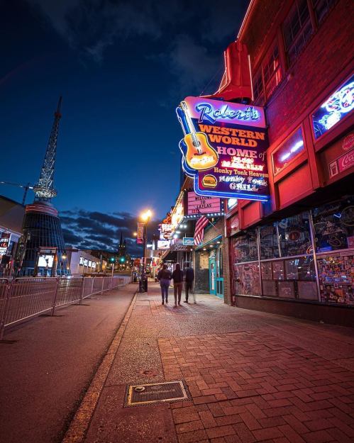 A vibrant street scene at night featuring a neon sign for Robert's Western World and a lively atmosphere.