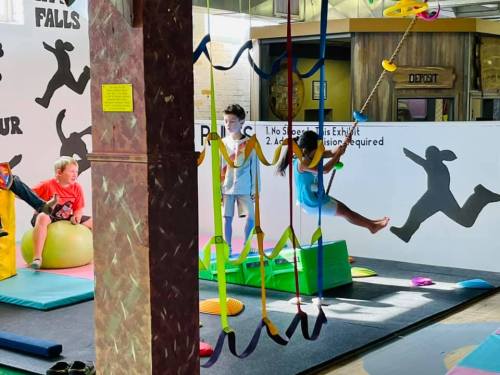 Children playing in a colorful indoor play area with climbing structures and swings.