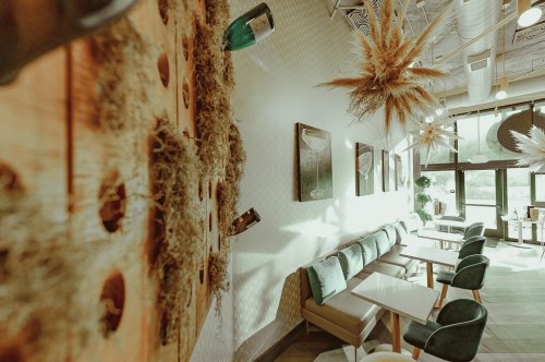 Cozy café interior with wooden accents, green plants, and natural light streaming through large windows.