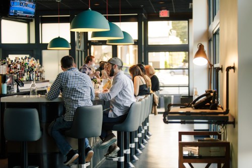 A lively bar scene with patrons seated at the counter, enjoying drinks under stylish pendant lights.