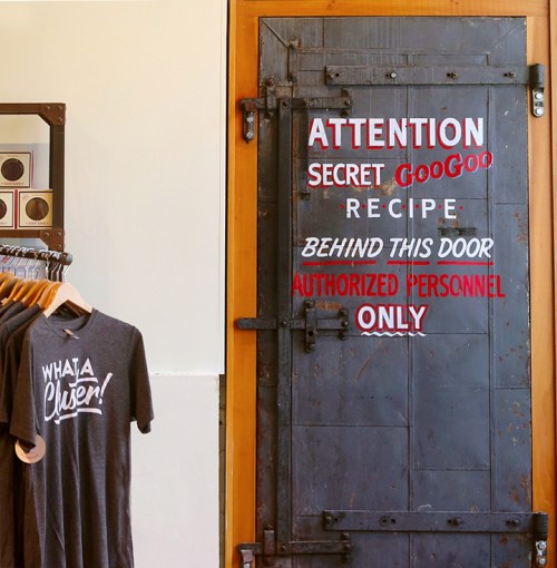 A door with a sign reading "Attention: Secret GooGoo Recipe. Behind this door: Authorized Personnel Only." Next to it, a shirt hangs.