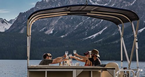 A group of friends toasting with drinks on a boat, surrounded by mountains and a serene lake.