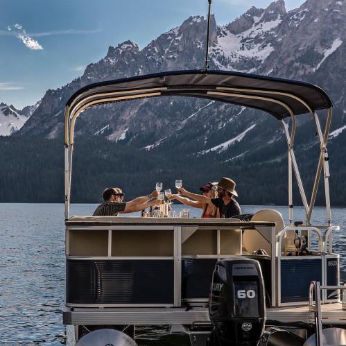 A group of friends toasting with drinks on a boat, surrounded by mountains and a serene lake.