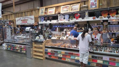 A busy shop display with various items, including knives and souvenirs, and customers browsing at the counter.