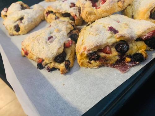 Freshly baked scones with berries, dusted with sugar, on a parchment-lined baking tray.