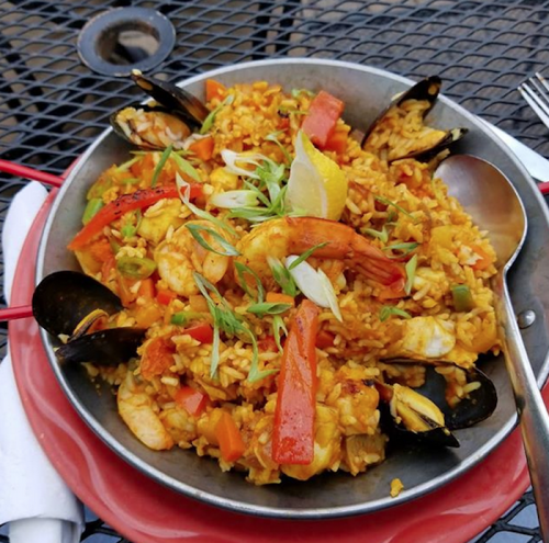 A vibrant seafood paella with shrimp, mussels, bell peppers, and green onions served in a metal dish.