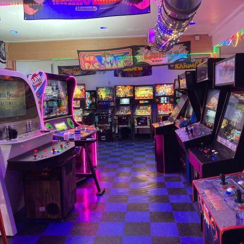 A vibrant arcade filled with classic pinball and arcade machines, featuring colorful lights and a checkered floor.