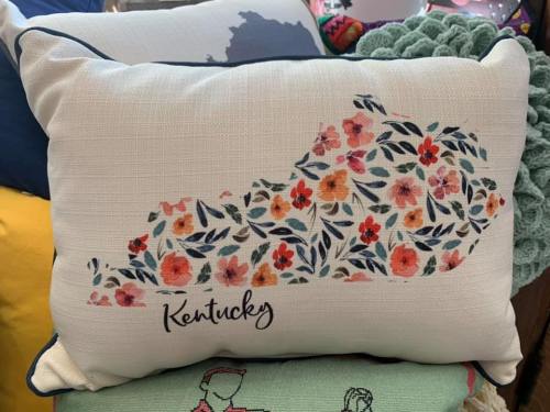 A decorative pillow featuring a floral design of the state of Kentucky with the word "Kentucky" written below.