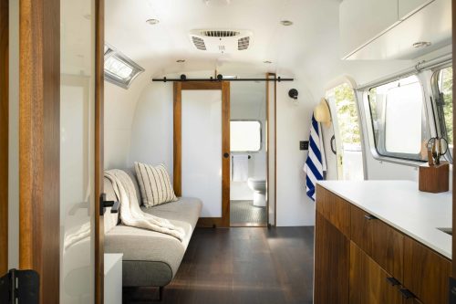 Cozy interior of a modern camper, featuring a sofa, wooden accents, and a sliding door leading to a bathroom.
