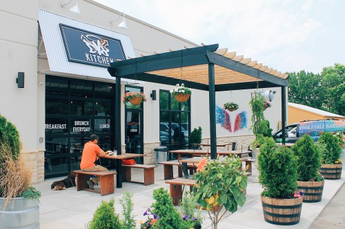 Outdoor dining area of a restaurant with wooden tables, hanging plants, and a bright, inviting atmosphere.
