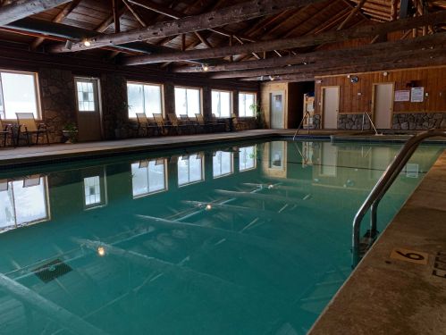 Indoor swimming pool with wooden beams, lounge chairs, and large windows, reflecting a calm, serene atmosphere.