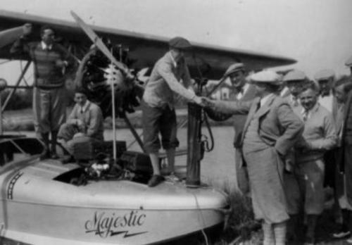 A historic black-and-white photo of men shaking hands near a vintage aircraft named "Majestic."
