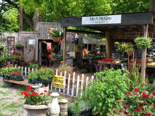A charming market with colorful flowers, wooden stalls, and a sign for local honey, surrounded by greenery.