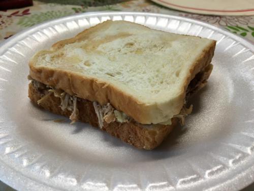 A simple sandwich made with two slices of bread and shredded meat, served on a paper plate.