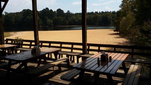 View from a wooden deck overlooking a sandy beach and calm lake, surrounded by trees under a clear blue sky.