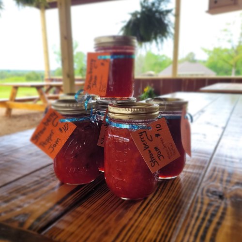 Five jars of strawberry jam with orange price tags, sitting on a wooden table outdoors.