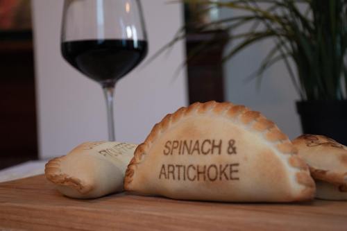 Three baked pastries labeled "Spinach & Artichoke" on a wooden board, with a glass of red wine in the background.