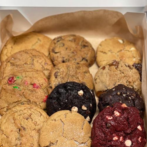 A box of assorted cookies, including chocolate chip, red velvet, and festive varieties, arranged on parchment paper.