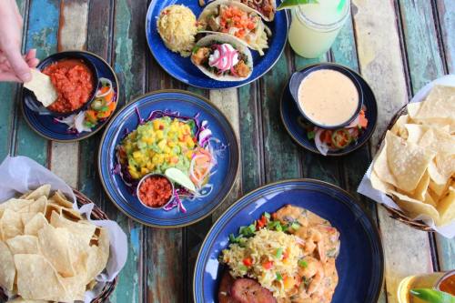 A vibrant spread of Mexican dishes, including tacos, rice, salsa, and tortilla chips on a rustic wooden table.