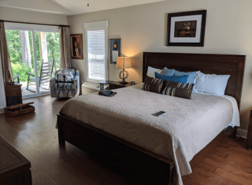 Cozy bedroom with a large bed, decorative pillows, a lamp, and a view of a deck through sliding glass doors.