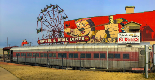 A vintage diner with a train car exterior, a large mural, and a nearby Ferris wheel in the background.