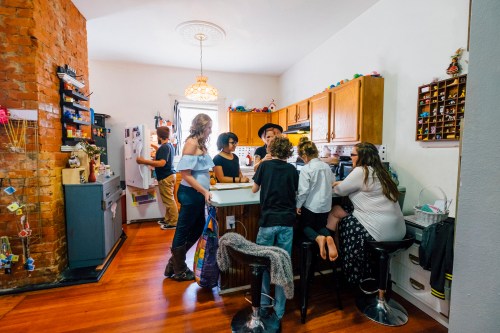 A lively kitchen scene with a group of people, including children and adults, gathered around a counter and interacting.