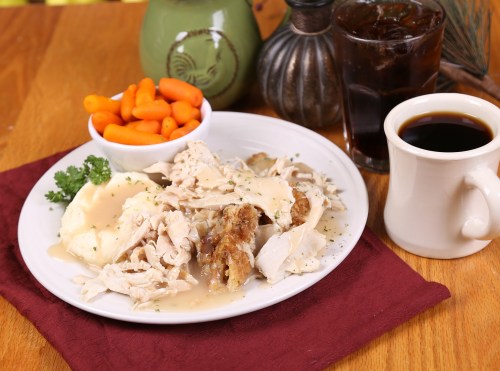 A plate of sliced turkey with gravy, mashed potatoes, and carrots, accompanied by coffee and a glass of soda.