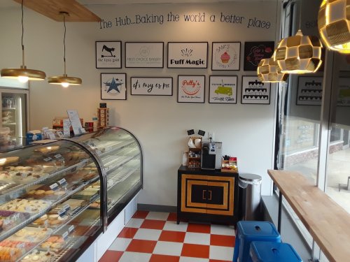 Cozy bakery interior with display case of pastries, wall art, and a coffee station, featuring a checkered floor.