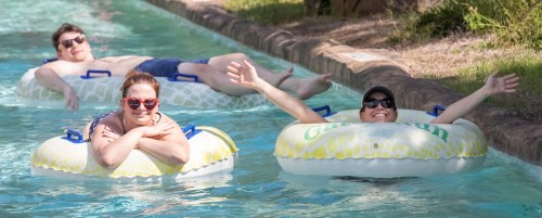 Three people relax on inner tubes in a lazy river, enjoying the sun and water on a warm day.