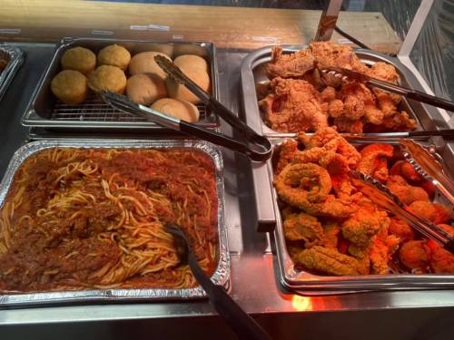 A buffet display featuring spaghetti with marinara sauce, fried chicken, hush puppies, and fried shrimp.