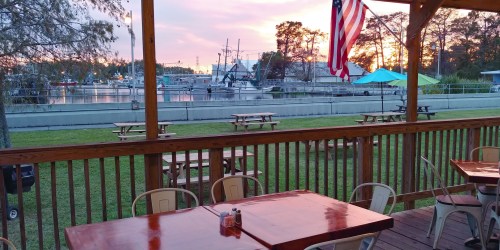 View of a marina at sunset, with picnic tables and an American flag in the foreground.
