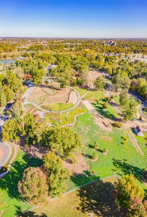 Aerial view of a park with winding paths, green lawns, and trees under a clear blue sky.
