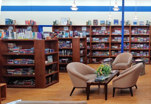 A cozy bookstore interior with wooden shelves filled with books and two armchairs around a small table.
