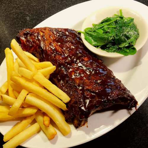A plate featuring BBQ ribs, crispy French fries, and a side of fresh spinach.