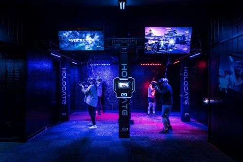 A dimly lit virtual reality arcade with players wearing headsets, illuminated by colorful lights and screens displaying games.