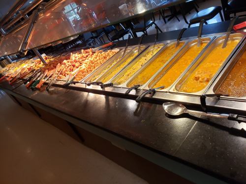 A buffet line featuring various trays of food, including meats and sauces, under warm lighting.