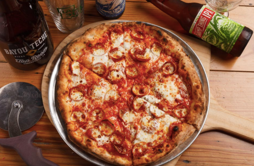 A freshly baked pizza with cheese and pepperoni, served on a wooden board with drinks in the background.