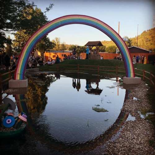 A colorful rainbow arching over a pond, with people gathered around in a park setting.