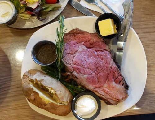 A plate featuring a large slice of prime rib, green beans, a baked potato with butter, and a side salad.