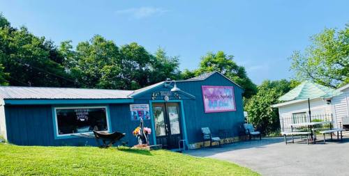A blue building with a sign reading "Dancing Springs Bed & Cafe," surrounded by greenery and outdoor seating.