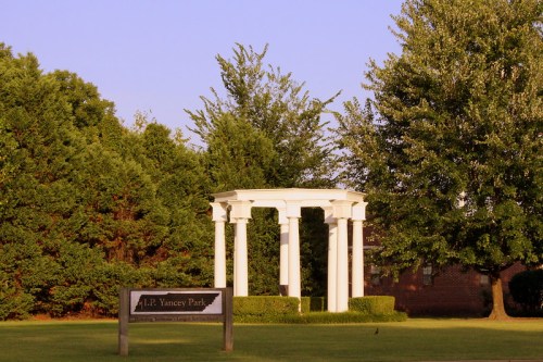 A white gazebo surrounded by trees in A.P. Yancey Park, with a sign marking the park's name in the foreground.